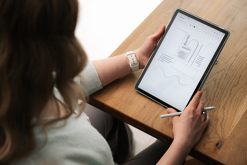 Blick über Corinnas Schulter auf ein Tablet